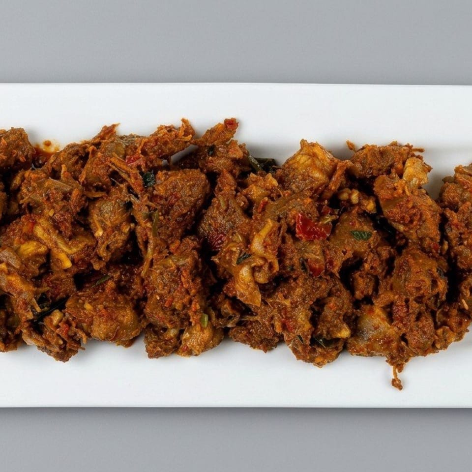 Spiced, crispy fried meat pieces garnished with chilies and curry leaves on a rectangular white plate.